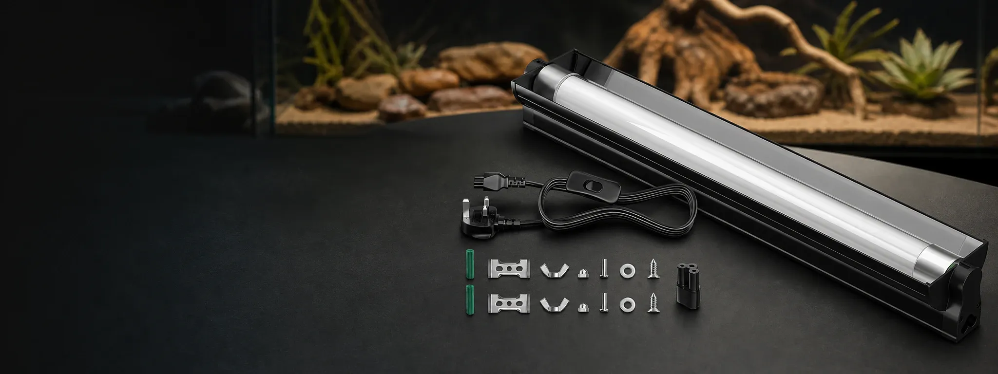 Complete UK reptile UVB lighting kit including fluorescent tube, power cord with UK plug and switch, mounting brackets, screws, and wall plugs, displayed on a black surface with a blurred desert-style terrarium background.
